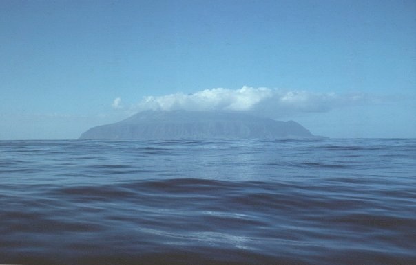 Tristan da Cunha from the sea, a volcanic island rising from the horizon with cloud across its peak.